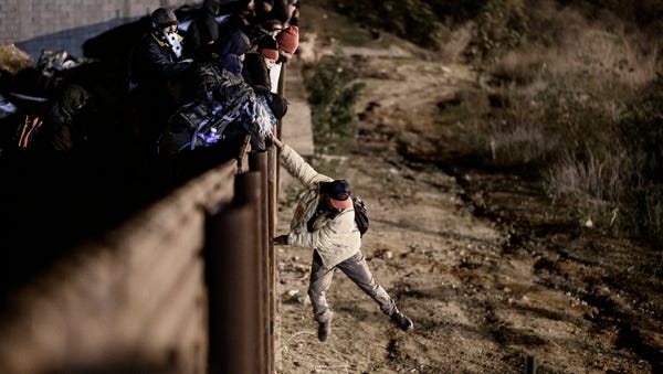 A migrant jumps the border fence to get into San...