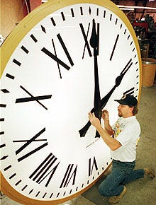 Harry Mantos, a worker at the Electric Time Co. in Medfield, adjusts the hands on a 7-foot-tall clock being built for the Twin Stacks Center in Dallas, Pa.
