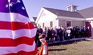 Cub Scout Matt Oickle, Pack 76, keeps an eye on the flag in front of the new Harwich Community Center yesterday as a crowd lines up for a first look at the site during a dedication ceremony yesterday.