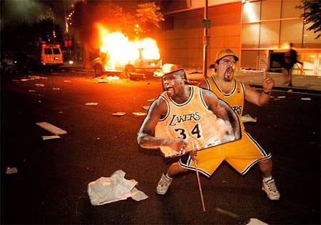 A fan celebrates outside the Staples Center with a large cut out of Shaquille O'Neal as a news vehicle burns after the Los Angeles Lakers defeated the Indiana Pacers in Game 6 of the NBA Finals Monday in Los Angeles. A celebration of the Lakers' first championship in 12 years deteriorated into mayhem as hundreds of fans torched two police cars, vandalized businesses and set dozens of small bonfires in streets.
