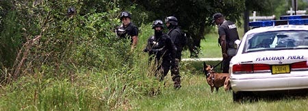 Members of a Plantation Police SWAT team enter the woods near the home of Carl Lawson on Tuesday in Plantation, after the 63-year-old man fired shots at state inspectors. Liz Compton, a Florida Department of Agriculture spokeswoman in Tallahassee, said the inspectors were there to check whether the trees on the property are infected with citrus canker, a threat to the state's citrus industry.
