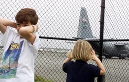 Young Vineyard vacationers Will Stabler, 7, and his sister Charlotte, 3, protect their ears against the roar of an Air Force transport jet leaving Martha's Vineyard Airport yesterday after dropping off motorcade cars for the president's visit. The Stablers are vacationing from Washington, D.C.