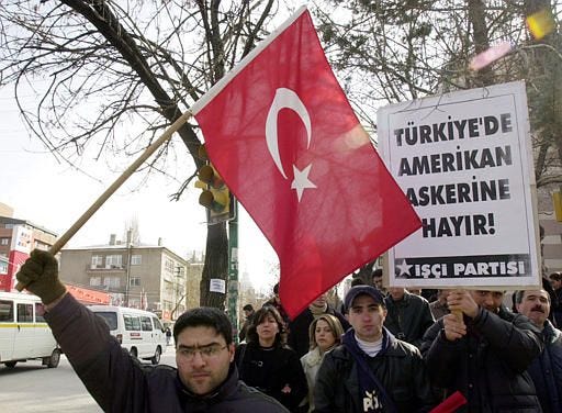 Turks, members of the leftist Workers Party, holding national flags and a banner that reads " No to American soldiers in Turkey " march in front of the U.S. embassy in Ankara during a protest rally on Monday, Feb. 17, 2003. A recent poll shows that 94 percent of Turks are against a war on Iraq.