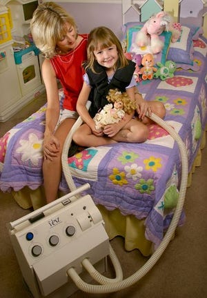 Five-year-old Ashleigh Godfrey, who was diagnosed with cystic fibrosis when she was 6 months old, poses in her bed with her mom, Carrie Godfrey. Ashleigh is wearing a specialized vest that is used for respiratory therapy.