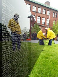 Vietnam War veteran Eddie Glenn is reflected in "The Wall That Heals" yesterday as he helps other volunteers, including Steve Brothers, right, set up the replica of the Vietnam Veterans Memorial on the Hyannis Village Green.