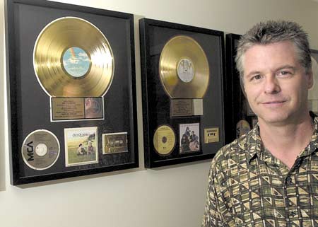 John Hichborn of Records on the Wall, Inc,. stands with the gold and platnum records that hang on his Exeter office wall from soundtracks of movies and shows that he has worked on.