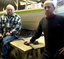 Boat builder Bob Manni, left, and Greg Egan, vice president of the Crosby Yacht Yard in Osterville, in front of a Wianno Senior sailboat under construction yesterday at the boatyard. Egan says he has already received requests from owners who want to replace boats destroyed in the Dec. 12 five-alarm fire.