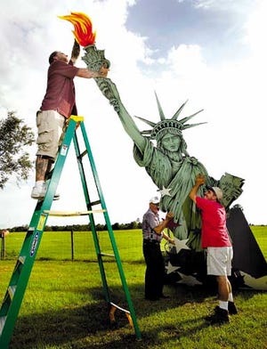 Wayne Lessard reaches from a ladder Saturday to adjust the lights on a 16-foot Statue of Liberty replica he built as Russell Moore, ground from left, and Robert Melfi help hold it up. The plywood lady liberty was built in preparation for a party today in Newberry for Independence Day.