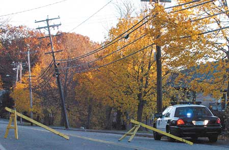 A poilce officer sits in front of a leaning telephone pole on Sagamore Avenue in Portsmouth on Friday.