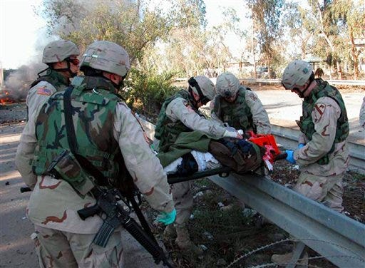 In this photograph released by the U.S. Army, soldiers from the 1st Cavalry and 10th Mountain divisions lift a wounded Iraqi civilian over a highway guard rail while evacuating him to a local hospital Monday. The civilian was severely wounded when a car bomb exploded near a checkpoint to the International Zone in central Baghdad.