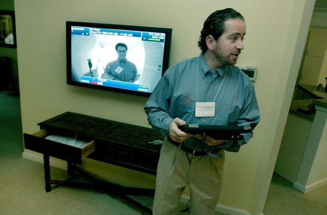 Youssef Kaddoura, a research assistant with the computer science and engineering department at the University of Florida, demonstrates the Smart House technology Friday morning in the living area of the new home for tour groups. The background screen shows someone at the door and allows the occupant to open the door with a voice command.