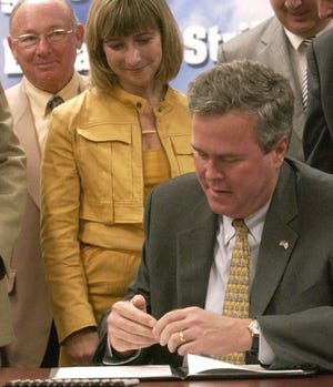 Gov. Jeb Bush on Monday in Pensacola prepares to sign into law a bill that will give Floridians a sales tax break on certain hurricane preparation items. Escambia County Commissioner Bill Dickson, left, and state Rep. Holly Benson, R-Pensacola, a co-sponsor, look on.