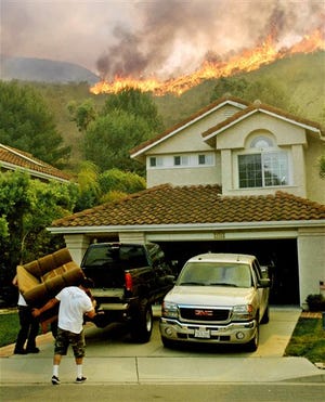 Two men load a couch into a pickup truck as flames crest a ridge behind their home in the hills near Ventura, Calif., on Friday.