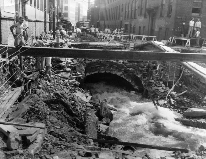 Water roars through a section of the Blackstone Canal during flooding on Union Street in Worcester as utility workers string cables in this 1955 photo.