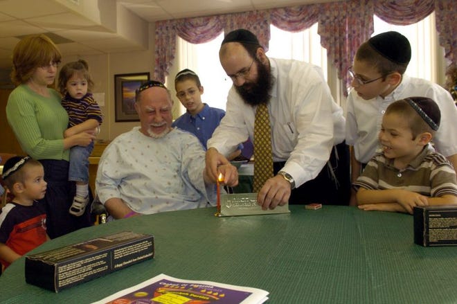 Rabbi Chaim Steinmetz, third from right, helps Abe Abraham light a small menorah to celebrate the first day of Hanukkah on Sunday at Sarasota Memorial Hospital. With Steinmetz is his family, Yossi, 3; wife Sara, holding Shmuli, 1; Levi, 11; Zev, 13; and Mendy,