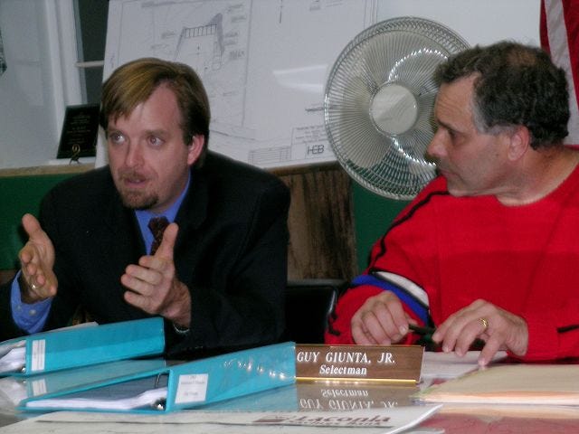 SELECTMAN GUY GIUNTA JR., right, listens as Selectman Andrew Livernois discusses the Official Ballot Act at a public hearing in the Sanbornton town offices Wednesday evening.