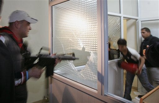 A Fatah militant uses his rifle to smash a window inside the Palestinian parliament building in the West Bank town of Ramallah, Monday, June 12, 2006.