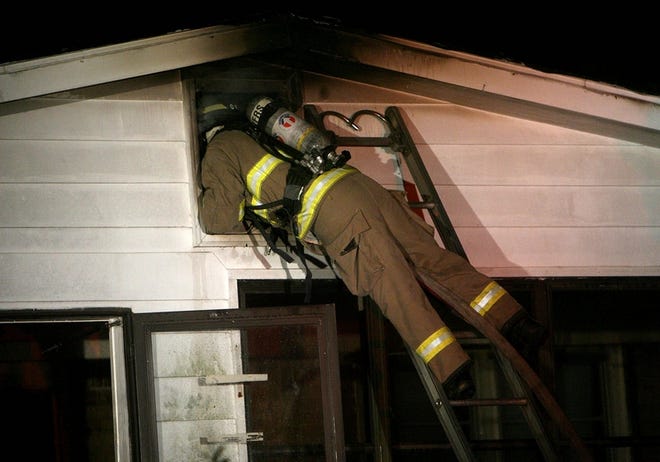 A Tuscaloosa firefighter attempts to extinguish a fire through the attic of a house that caught fire Friday night in Holt.