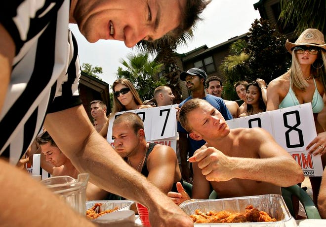 Jason Bowman of AOI Media, top, counts the discarded wings of Ryan Preston(third from left), 21, a University of Florida student, Saturday, July 7, 2006. A crowd of people gathered around the table of contestants at Campus Lodge pool to watch as six men devoured as many wings as possible in 20 minutes. Gatorfood.com and AOI Media sponsored the Hooters Wing Eating contest. At far right is Classmates Calendar girl, Turi Stevens, 20.