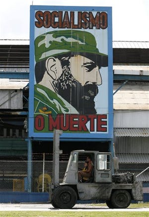 A man with a child rides in a forklift as they pass a factory showing an image of Fidel Castro that reads "Socialism or Death" in Havana, Cuba, Wednesday, Aug. 2, 2006.