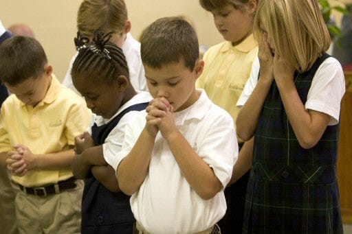 Jonas Reilly, 6, center, prays with other students at the opening of the school day and school year at Ambleside School of Ocala on Monday. The new school is in a building at First United Methodist Church on East Silver Springs Boulevard in Ocala.