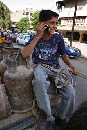 An Iraqi boy talks on his cell phone as he ferries gas cylinders on a horse cart in Baghdad, Iraq, on Aug. 13. Sending text messages and personalizing ringtones has become the highlight of entertainment in Baghdad, with the city's restaurants, cafes and cinemas closed.