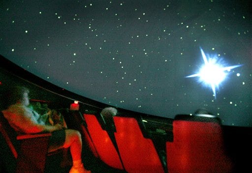 A 30-second-exposure photograph shows attendees watching in image of Pluto with its moons, right, during "To Pluto & Beyond!", a show at Barlow Planetarium on the University of Wisconsin-Fox Valley campus in Menasha, Wis. Pluto lost its status as the ninth planet of the solar system earlier in the day, and has been reclassified by the International Astronomical Union as a "dwarf planet."