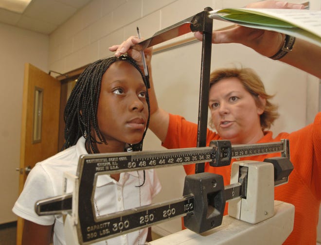 Shuman Middle School athletic director Leslie Corley measures the height and weight of 7th grader Shacarrie Heyward who intends to try out for the school softball team.