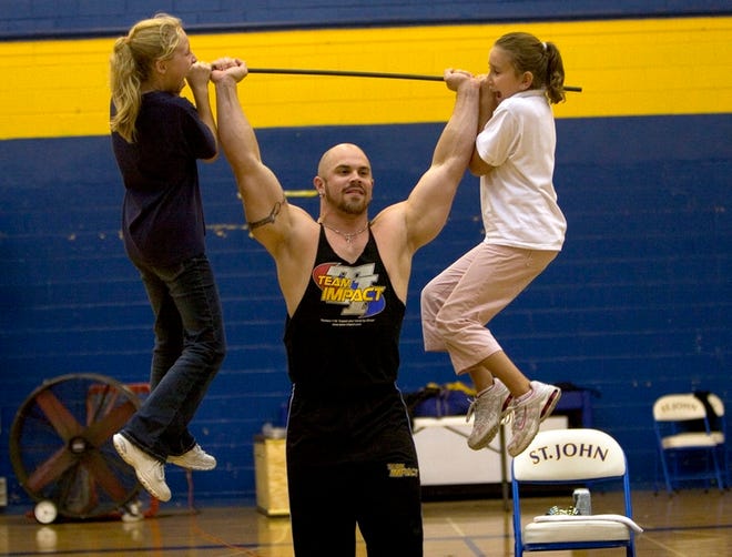 Team Impact's Aaron Brewer picks up sixth-graders Josie Devine, left, and Bailey Nookes during a performance Friday at St. John Lutheran.