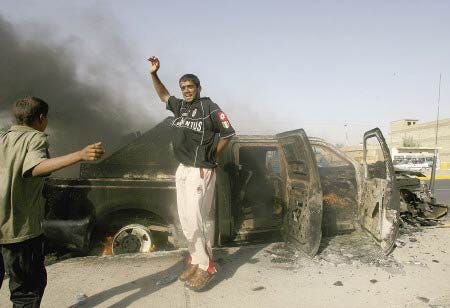 Iraqis dance in front of a burnt vehicle, in Baghdad, Iraq, on Monday. A roadside bomb targeting a convoy of foreign private security guards exploded late on Sunday evening damaging one of their vehicles and injuring two occupants, police said.
AP photo