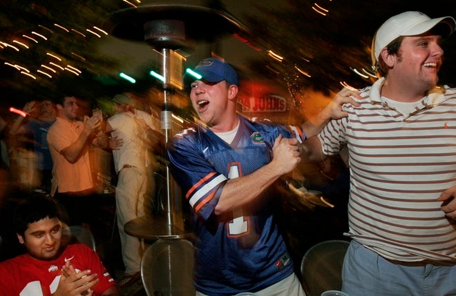 University of Florida students Adam Wright, center, and Matt Brooks Jr., right, celebrate at the Swamp restaurant on West University Avenue in Gainesville on Sunday. Ohio State fan Neil Desai, left, looks on.
