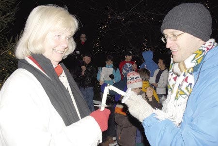 Ann Fisher, left, J.D. Bellamy pass the flame at Newmarket's candle lighting and caroling at the 18th annual Giving Tree Ceremony Saturday night.