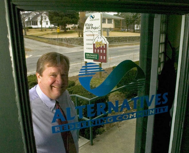 Dennis H. Rice is shown in front of his office at Alternatives Unlimited Inc. In the background is a sign noting the progress of the Whitin Mill project.
