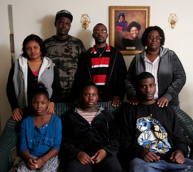 Clockwise from top left, Quita Hinton, Rafeal Nevels, David Hinton, Shirley Nevels, Dondrell Nevels, Tysherra Nevels and Tawana Nevels pose in front of a portrait of Shana Nevels at their 38th Place apartment on Friday. Shana Nevels died in a fire at the family’s home in Duncanville in November.