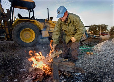 Construction worker Mark Ingram, builds a small fire from construction debris on Shepherd Rd. to warm himself this morning as temperatures dipped into the low 30's. Ingram was part of a crew laying underground pipe for a new housing development.