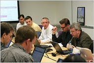 Two members of the Project Panama team, Mark Morrissey, center, and Brian Acton, right, leading the daily meeting in the “war room.”