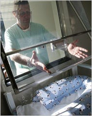 An orderly, Stefano Lorenzi, shows how to place an infant through a hatch into a heated crib.