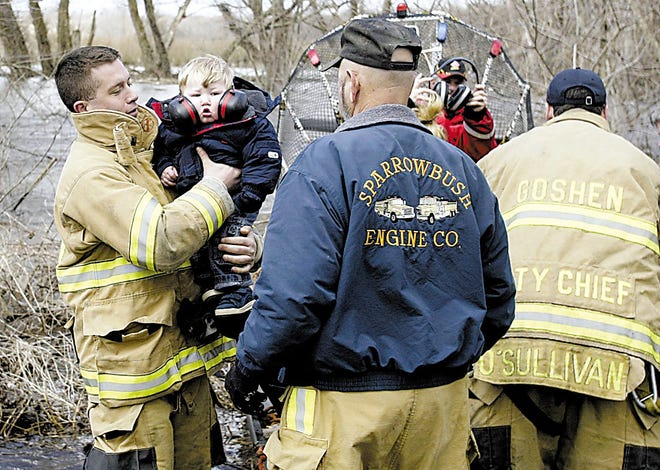 ABOVE: A Goshen firefighter holds Eric Faith, 1, yesterday after his family was rescued from their home on Celery Avenue in the Town of Goshen. The Wallkill River, in background, rose overnight and cut off families on Celery Avenue.