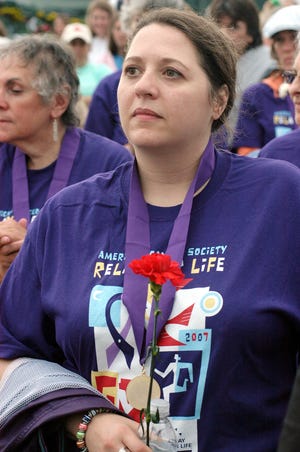 Suzanne Rouvalis of Marshfield, a 10-year survivor of non-Hodgkin’s lymphoma, holds a red carnation while listening to speakers at the Marshfield Relay for Life Friday evening.