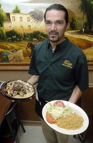 Sergio Mata, a waiter poses with one of El Patron's specialties, Pollo Hawaiano, served with a side of rice and salad.