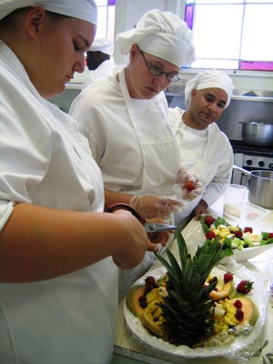 Chefs-in-training Cynthia Smith, left, and Jessica Cowan work on a fruit platter as Jose Quinones looks on. The three are among the first graduates of the Culinary Training Institute in Monticello.