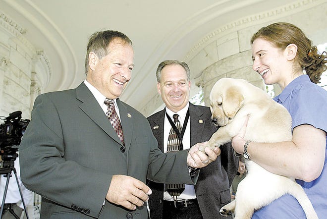 Orange County Executive Ed Diana greets Rachel Silverman of Guiding Eyes for the Blind, holding Pal, a yellow Labrador retriever puppy, as Orange County Legislator Greg Townsend watches yesterday during a news conference announcing a training center at SUNY Orange.