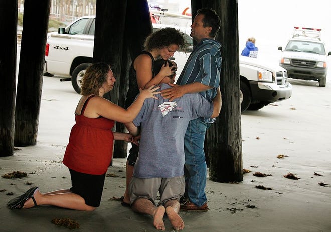 Ashby Fulmer, center, of South Carolina is surrounded by people under the Main Street Pier as they pray with him while Beach Patrol officers and other rescuers attempt to locate Ashby's son Barrett Fulmer who disappeared in the rough surf while swimming with boogie boards in front of the boardwalk area of Daytona Beach, Florida Monday afternoon, October 1, 2007. Barrett was apparently swimming with another man who also was caught up in the surf. The other swimmer made it safely to shore while Barrett did not. Rescuers called off the search as the sun set. Offically the Beach patrol is not classifying this case as a drowning.(The Daytona Beach News-Journal, Nigel Cook)