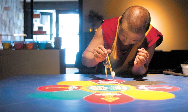 Tenzin Yignyen uses a compass to route sand into a more precise circle. At left are cups of colored sand that he will use in completing the work.