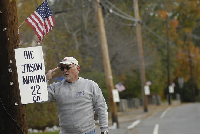 Roger Gandini, of Holliston, salutes one of over 500 posters yesterday morning with the name of a soldier killed in action in Iraq or Afghanistan. Gandini, an Army veteran, said he salutes each name he puts up the poster out of respect for the fallen soldiers and their families.