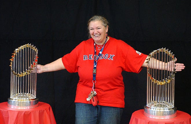 A delighted Martha Kempe of Milton, a Milton schoolteacher, poses with the Red Sox 2004 and 2007 World Series trophies at Sunday’s toy drive held in memory of Ciara Durkin and benefiting Cradles to Crayons.