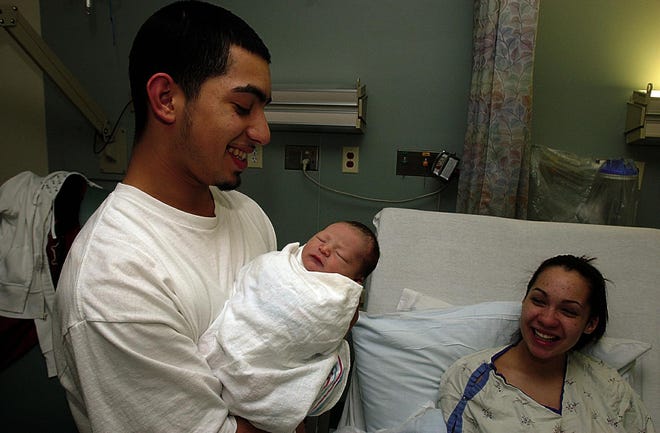 Jeff Montenegro, left, holds his new son as the baby's mother, Tiffany Hollinger, looks on from her bed at Morton Hospital in Taunton. The infant is the first baby born in Greater Taunton in 2008.