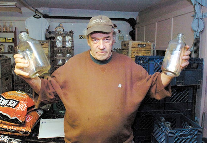 Robert Briggs with two of the many empty milk bottles at his farm, Shady Oaks, in Medway, Tuesday.