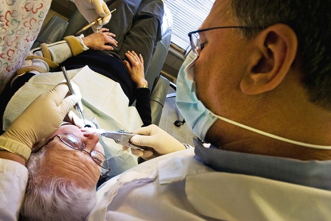 Dr. Dennis Lewis, right, repairs an old filling on patient Kay McClory at the Dental Aid office in Longmont, Colo.