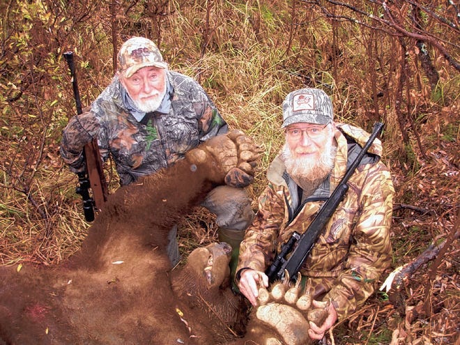 WAYNE SIMONS, LEFT, holds up a paw of the massive brown bear he hunted on a fall trip to Alaska as outfitter Phil Shoemaker helps out. The bear was over 10 feet long and 1,300 pounds.